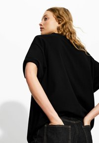 T-shirt nera oversize con maniche corte arrotolate, tessuto morbido, vestibilità rilassata, abbinato a jeans in denim scuri a vita alta.