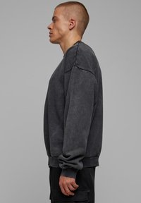 Felpa oversized grigio antracite realizzata in tessuto morbido, con maniche lunghe, scollo a girocollo e polsini e orlo a costine.