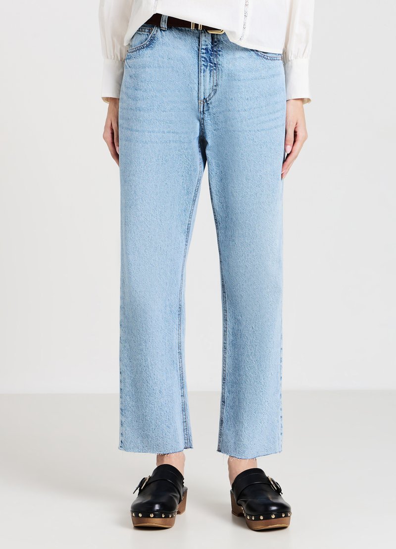 Jean droit bleu clair en denim, avec un ourlet effiloché et une légère décoloration. Associé à des sabots noirs à semelles en bois.