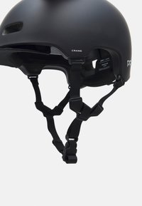 Caspolo nero con finitura opaca, dotato di aperture di ventilazione, cinturini regolabili e un logo. Imbottitura interna visibile per il comfort.