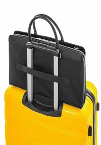 Czarna torba na laptopa o gładkiej fakturze przymocowana do błyszczącej żółtej walizki z twardą powłoką, charakteryzującej się żłobionym wzorem i chowanym uchwytem.