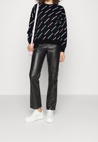 Felpa nera con motivo di testo colorato, abbinata a pantaloni in finta pelle neri e sneakers bianche. La borsa rosa aggiunge un tocco delicato.