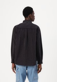 Black and white striped long-sleeve shirt with button cuffs and a back yoke detail, made of a textured fabric. Casual fit, rounded hem.