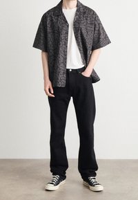 Zwart met een patroon kortebloemig overhemd met een luipaardprint, een witte T-shirt eronder, zwarte jeans en zwarte sneakers. Matte textuur, casual pasvorm.