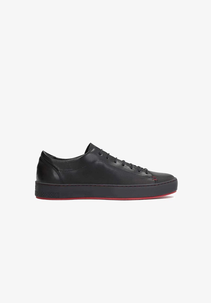 Adidași din piele neagră cu vârf rotund, talpă plată și accente roșii. Caracteristicile includ un design cu șireturi și cusături laterale contrastante.