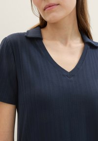 Top de cuello en V azul marino con un diseño acanalado texturizado, mangas cortas y cuello con solapas. Fabricado en un tejido flexible para mayor confort.