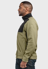 Fleecejacke in olivgrün mit schwarzen Akzenten, Reißverschluss vorne, hoher Kragen und Seitentaschen. Glatte Textur, anpassungsfähige Passform.