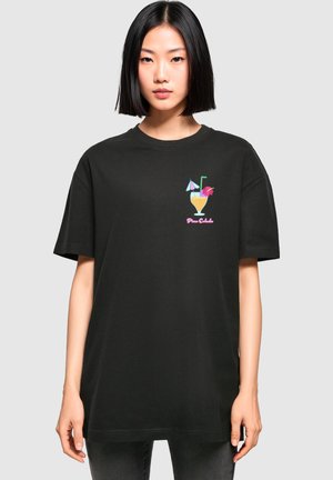 Black oversized t-shirt made of cotton featuring a colorful piña colada graphic on the chest with decorative elements like umbrellas and flowers.