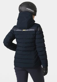 Dunkelblaue, wattierte Jacke mit Kapuze, ausgestattet mit einem glänzenden schwarzen Streifen über den Schultern und goldenen Logo-Akzenten. Geeignet für Aktivitäten im Freien.