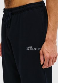 Marineblaue Jogginghosen aus weichem Material mit elastischem Bund und Kordelzug. Enthält weißen gestickten Text am linken Oberschenkel.