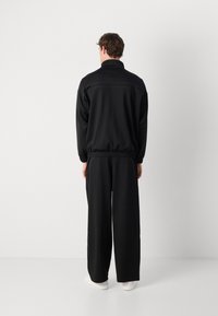 Fato de treino preto com uma jaqueta zipada de colarinho alto e punhos elásticos, combinado com calças de pernas largas. Tecido suave com detalhes mínimos.
