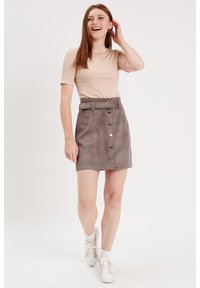 Haut côtelé beige à manches courtes. Mini-jupe en suède gris avec taille ceinturée, fermeture à boutons sur le devant et texture lisse. Baskets blanches.