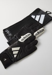 Gants de gardien de but de football noirs avec des accents blancs, dotés d'une sangle élastique, de paumes texturées et du logo Adidas visible sur les doigts.