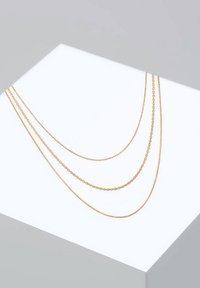 Gold layered necklace featuring three chains of varying lengths and styles. Smooth, round, and textured links on a light background.