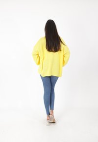 Maglione oversize giallo lavorato a maglia, vestibilità comoda, maniche lunghe, abbinato a jeans aderenti blu e mules con tacco trasparente. Siluetta semplice, dettagli minimi.
