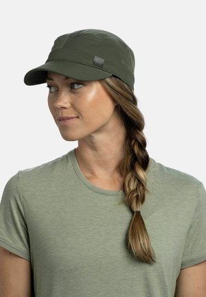 Mujer con cabello largo trenzado que lleva una gorra verde oliva y una camiseta verde oliva a juego, mirando hacia su izquierda sobre un fondo blanco.