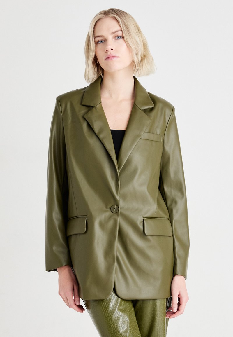 Olijfgroene faux leren blazer met een notch-kraag, enkele knoopsluiting, twee voorzakken en een relaxte pasvorm. Zachte textuur en minimale details.