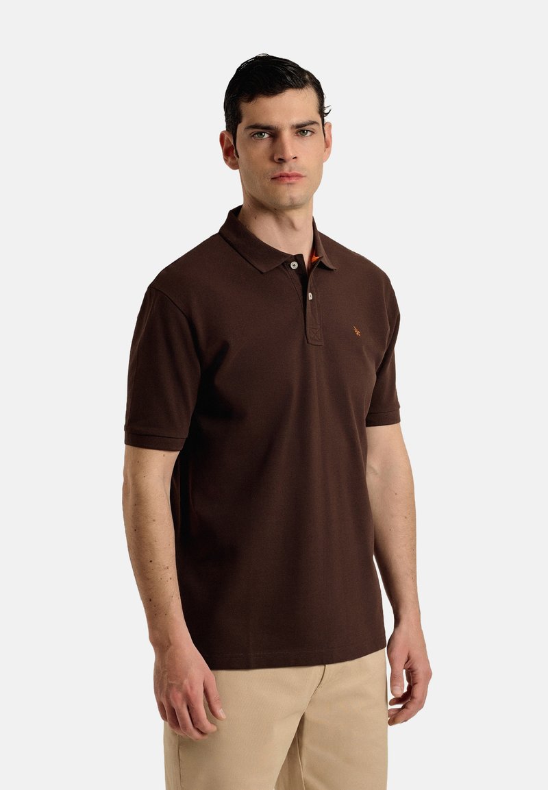 Camisa polo marrón de algodón, con cuello, mangas cortas y un detalle naranja en el cuello. Incluye un pequeño logo en el pecho.
