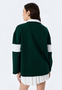 Felpa verde con un colletto bianco e una banda bianca sulle maniche. Texture morbida, vestibilità comoda e orlo posteriore leggermente più lungo.