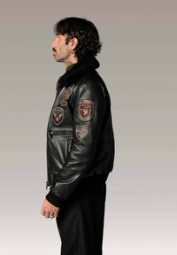 Veste pilote en cuir noir avec un col en fourrure, plusieurs patchs brodés sur la poitrine et les manches, et des poignets côtelés.