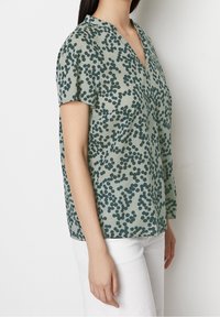 Blouse à manches courtes vert clair avec un motif ludique à pois verts foncés, dotée d'un col en V et d'une coupe ample. Texture de tissu lisse.