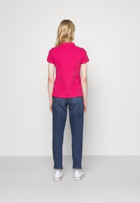 Fuchsia Poloshirt mit kurzen Ärmeln, kombiniert mit hochgeschnittenen blauen Jeans und weißen Turnschuhen; schlichtes Design, glatte Textur.