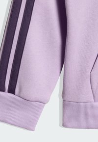Des manches de sweatshirt violet clair avec des rayures verticales violet foncé et violet clair le long d'une manche et des poignets côtelés.
