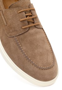 Brązowy zamszowy but sznurowany z precyzyjnym przeszyciem i białą gumową podeszwą, ukazany pod kątem, aby pokazać górę i przedni wzór.