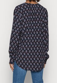 Bluse mit Blumenmuster in Marineblau, mit langen Ärmeln, gerafften Schultern und einem abgerundeten Saum. Das Material zeigt eine weiche, leichte Textur.