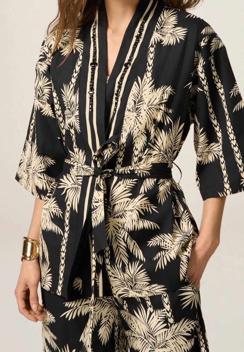 Robe in stile kimono nero e crema con motivo a foglie di palma, vita con cintura e maniche larghe. Tessuto liscio con decorazioni a perline.