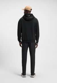 Felpa nera con cappuccio e orlo a coste, abbinata a pantaloni coordinati. Un cappello beige chiaro completa l'outfit, caratterizzato da colori neutri e design minimalista.