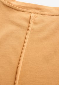 T-shirt en coton de couleur moutarde douce, avec un col arrondi, des manches courtes et une couture centrale allant du cou à l'ourlet.