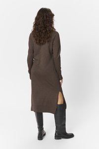 Robe marron à manches longues avec fentes sur les côtés, fabriquée dans un tissu doux. Associée à des bottes noires jusqu'aux genoux. Silhouette simple et épurée.