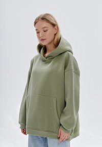 Felpa verde oversize in cotone, dotata di un grande cappuccio morbido, tasca frontale e spalle abbassate; polsini e orlo a coste.
