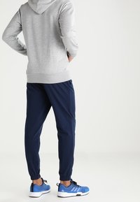 Sweat à capuche gris avec une couture dans le dos, joggeurs bleu marine avec poignets élastiques, et chaussures de sport bleues avec des accents noirs. Design simple et fonctionnel.