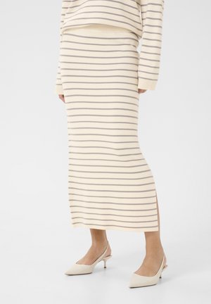 Vrouw draagt een crèmekleurige rok en trui met grijze horizontale strepen, gecombineerd met crèmekleurige slingback kitten heels.