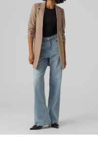 Béžové na míru ušité sako, černý přiléhavý top, světle modré džíny s vysokým pasem a širokými nohavicemi, a špičaté černé podpatky. Hladká látka s strukturovaným střihem.