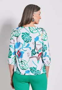 Bloemdruk top met groene, blauwe en rode ontwerpen op een witte achtergrond; 3/4 mouwen, ronde halslijn en lichtgewicht stof.