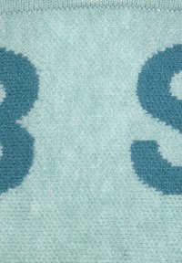 Türkiser Teppich mit weichem Material, der eine große, dunkelblaue stilisierte Zahl "8" und einen hellblauen Hintergrund zeigt.