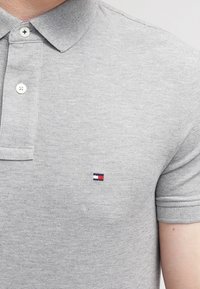 Polo gris en tissu texturé. Présente un col, trois boutons et un petit logo brodé sur la poitrine.