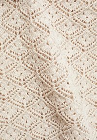 Gebreid textiel in lichtbeige met een gestructureerd ruitpatroon, voorzien van opengewerkt detail dat een zachte en luchtige uitstraling creëert.