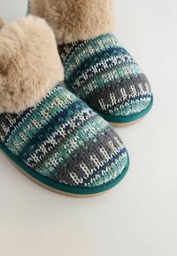 Zapatillas de punto en color azul verdoso, verde y gris con un ribete de piel sintética y un patrón texturizado. Suela de goma para mayor tracción. Acentuadas con hilo blanco.