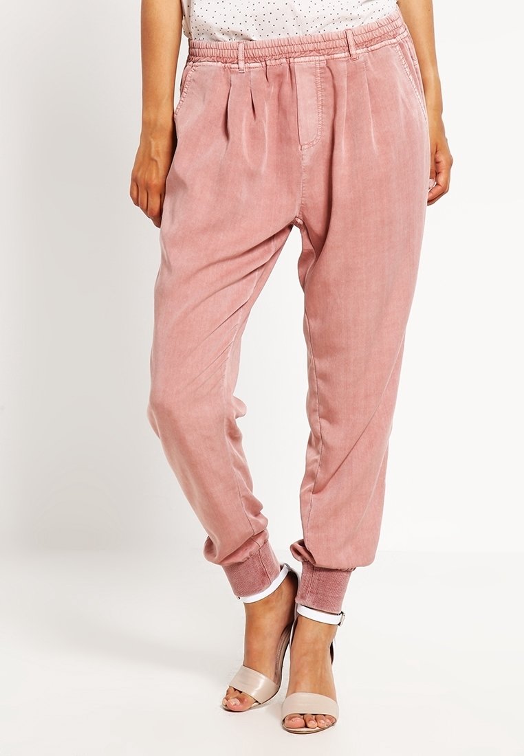 Pantalons de jogging rose avec une taille élastique et des poignets ; design plissé sur le devant ; tissu doux avec une texture lisse ; associés à des sandales de couleur claire.