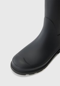 Black rubber boot with a rounded toe, smooth texture, and a thick tread sole. The design is simple with no visible hardware or patterns.
