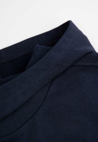 Granatowa bawełniana koszulka z okrągłym dekoltem, charakteryzująca się gładką teksturą i płaskimi szwami. Złożony kołnierz prezentuje czyste wykończenie.