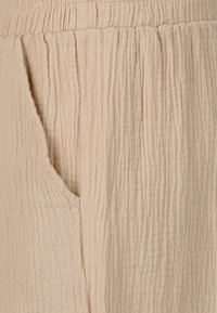 Beige, strukturerad tyg med vertikala rynkor; inkluderar en sidoficka och ett elastiskt midjeband för komfort och passform.