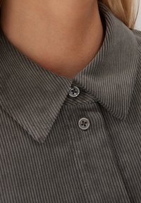 Camicia in velluto a righe grigia con colletto a punta, due bottoni coordinati e texture a righe verticali. Vista ravvicinata che mette in evidenza i dettagli del colletto.