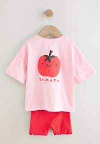 Krátké růžové tričko s červenou grafikou rajčete a nápisem "tomato" dole, doplněné červenými žebrovanými šortkami s volánkovými lemy.