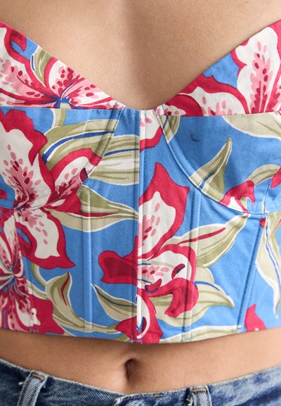Blomstrete crop topp med blå bakgrunn, som har røde og grønne blomsterdesign, v-hals og strukturerte sømmer for en tettsittende design.