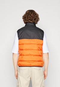 Pánská puffer vesta s černou horní částí a oranžovou dolní částí s prošívanou strukturou. Vysoký límec a bezrukávový design.